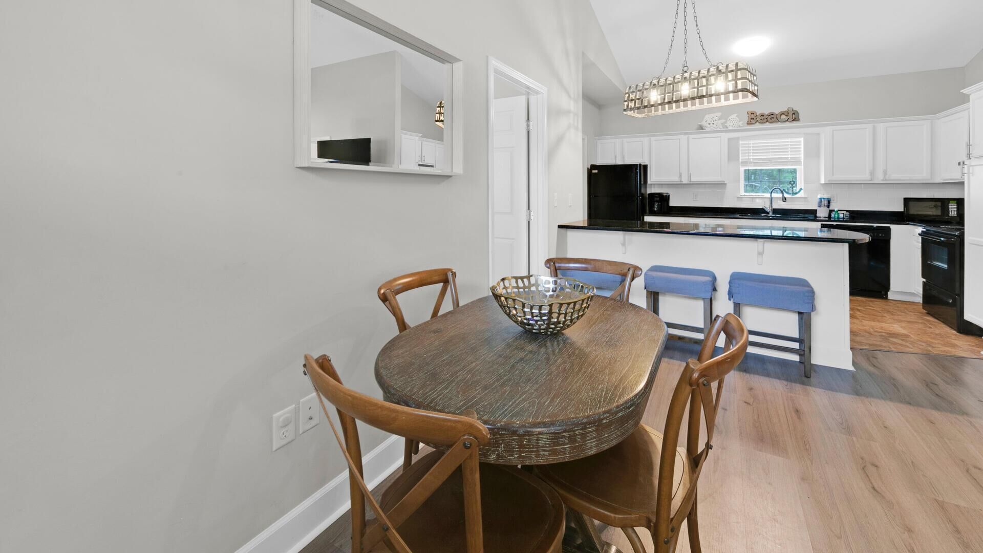 Een moderne keuken met witte kasten, een zwarte koelkast en een houten eettafel met vier stoelen.