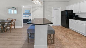 A modern kitchen with white cabinets, a black refrigerator, and a dining area with a glass-top table and wooden chairs. - Once Upon a Tide (Santa Rosa Beach)