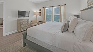 A bedroom with a bed, dresser, lamp, chair, and a TV on the wall. - Once Upon a Tide (Santa Rosa Beach)
