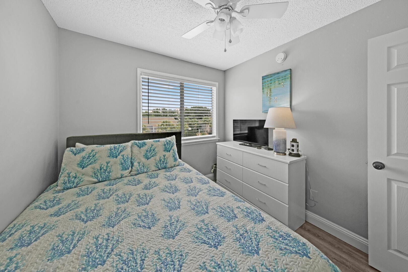 Une chambre à coucher comprenant un lit, une commode, un téléviseur et un ventilateur de plafond.