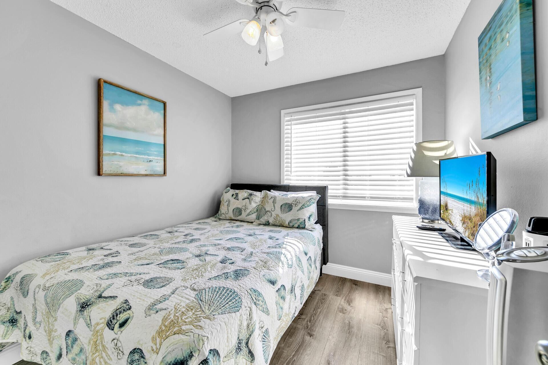Une chambre à coucher avec un lit, un bureau avec un ordinateur, un ventilateur de plafond et une fenêtre avec des stores.