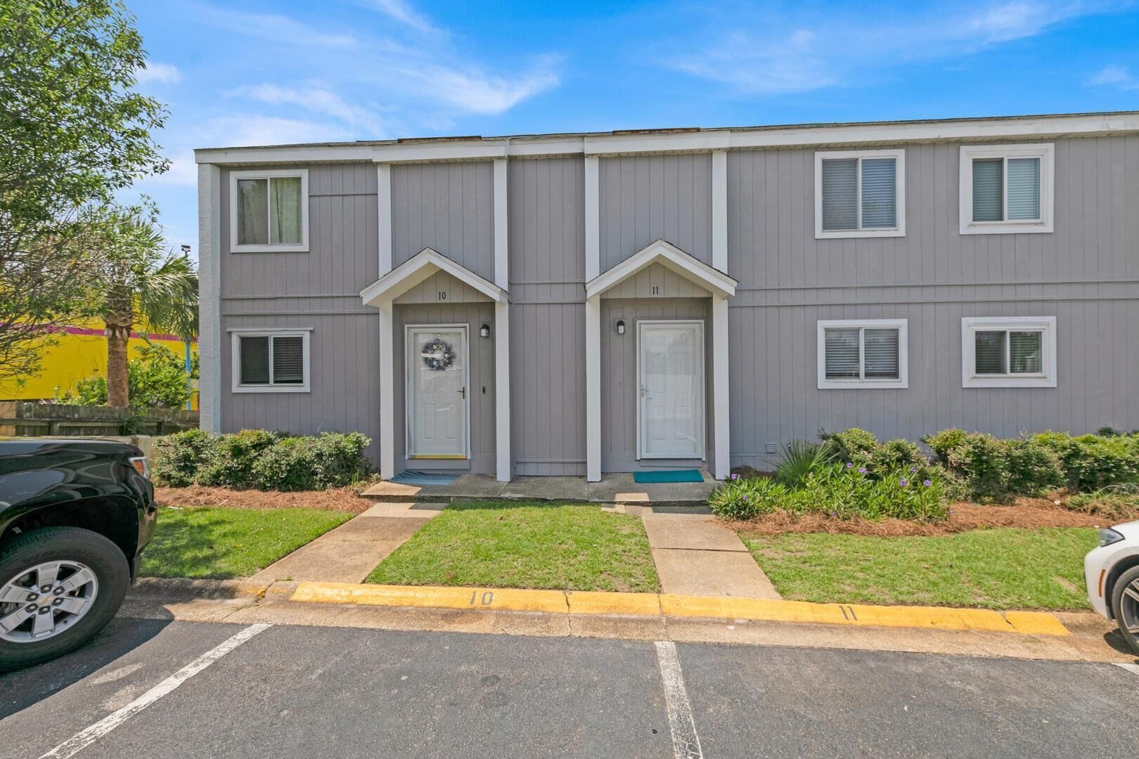 A two-story building with a symmetrical facade, numbered doors, and a parking lot in front.