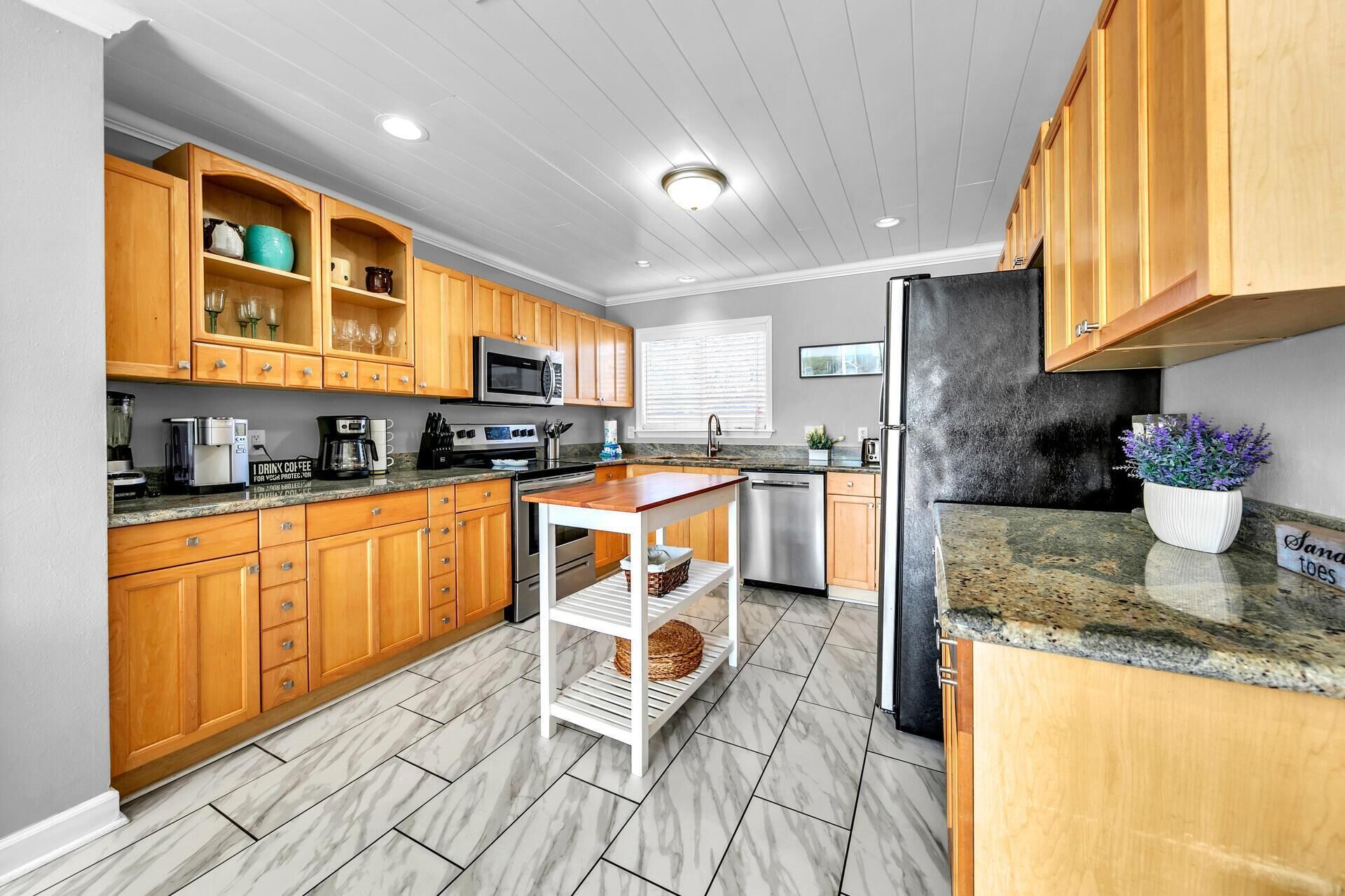 A modern kitchen with wooden cabinets, a granite countertop, stainless steel appliances, and a marble floor.