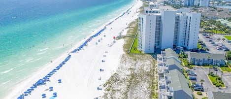 A beachfront hotel with multiple high-rise buildings, a long stretch of beach with umbrellas, and a clear view of the ocean.