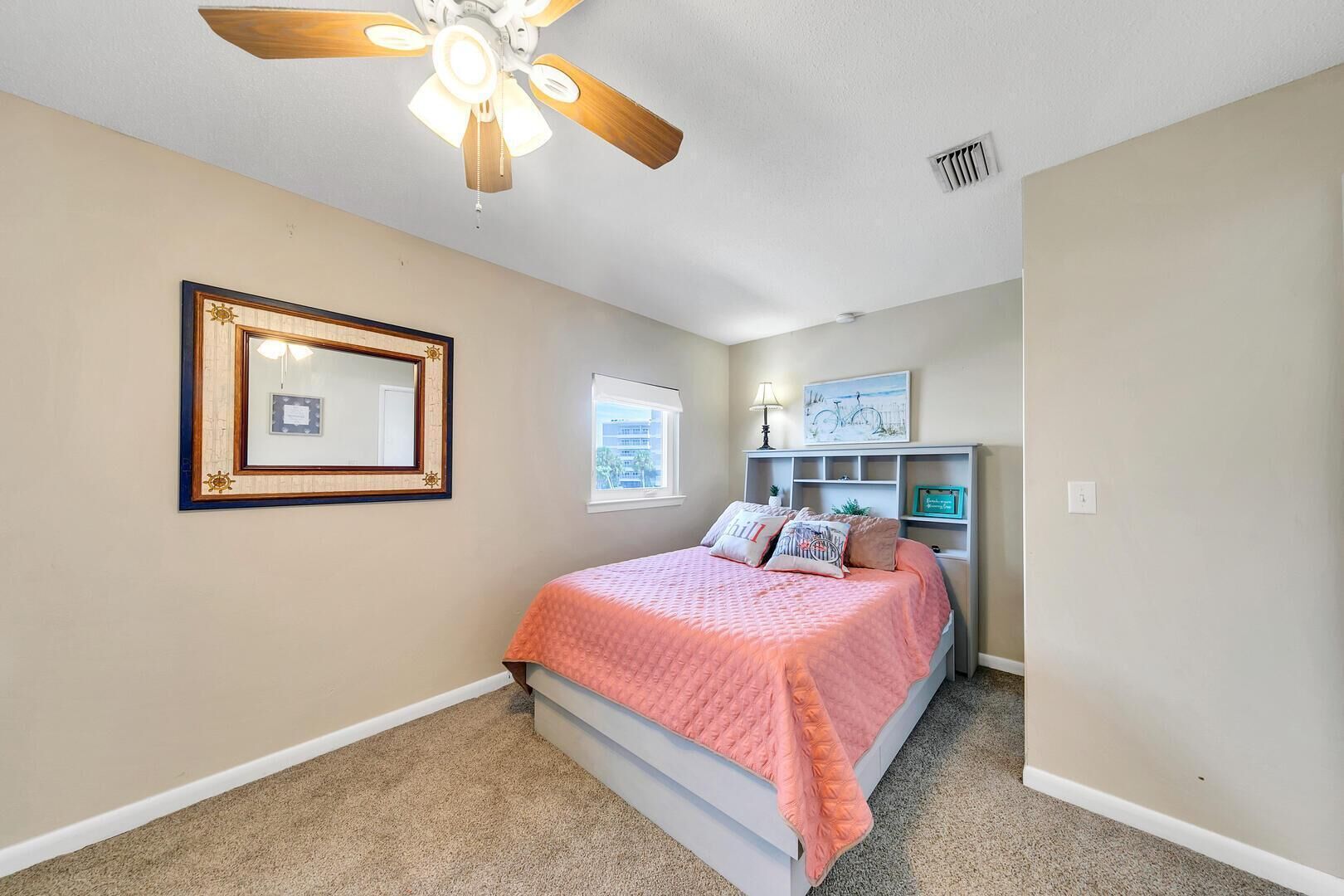A bedroom with a bed, a ceiling fan, a window, and a wall-mounted shelf with decorative items.