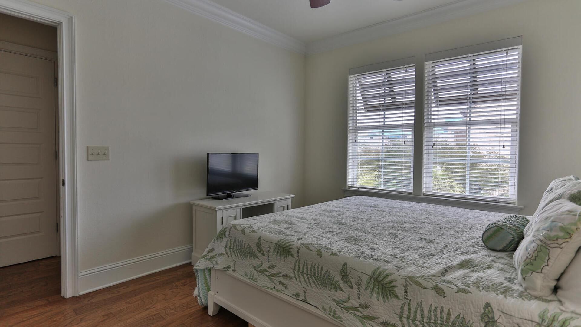 Une chambre à coucher avec un lit, un téléviseur posé sur une table de chevet et une fenêtre avec des stores.