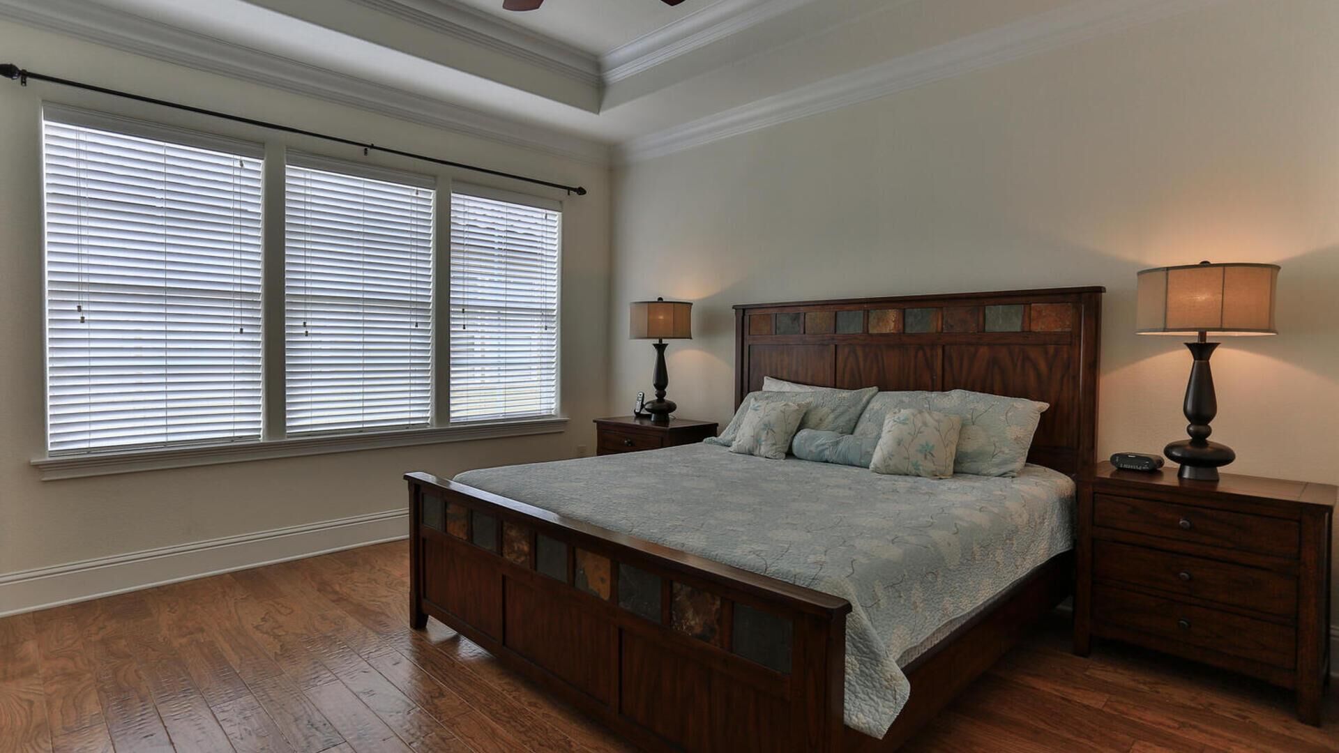 A bedroom with a wooden bed, two bedside tables with lamps, and a large window with blinds.