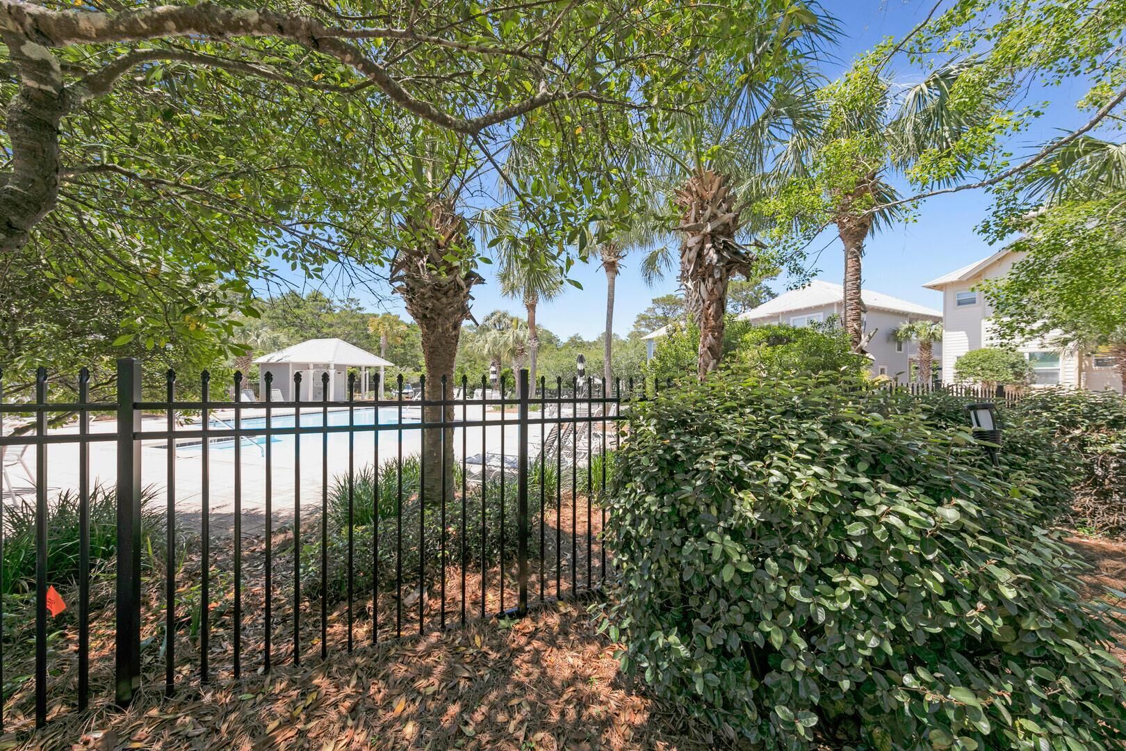 A fenced outdoor area with a pool, surrounded by trees and a well-maintained garden.