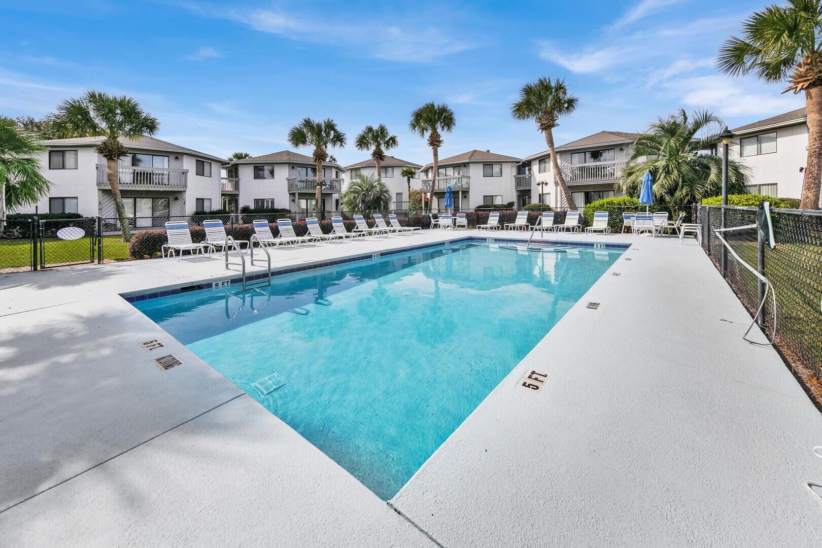 A rectangular swimming pool with a 5 FT depth marking, surrounded by lounge chairs and palm trees, with multi-story buildings in the background.