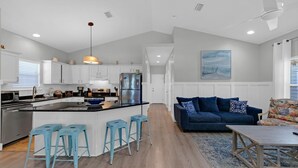 Een moderne keuken met witte kasten, een centraal eiland en blauwe barkrukken.