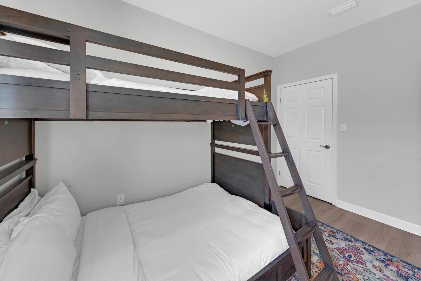 A bunk bed with a ladder, white bedding, and a door in the background.