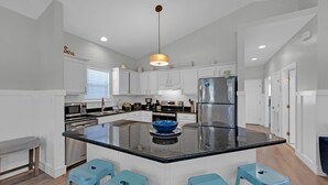 Een moderne keuken met witte kasten, een roestvrijstalen koelkast, een groot eiland met blauwe barkrukken en een hanglamp.
