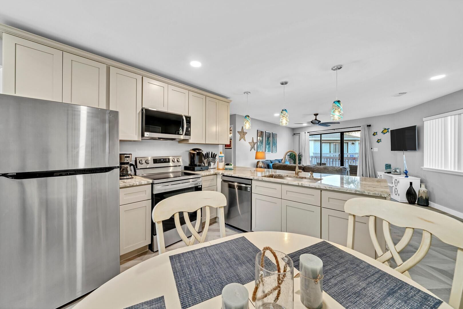 A modern kitchen with stainless steel appliances, a dining area with a round table and chairs, and a view of the living area through a glass door.