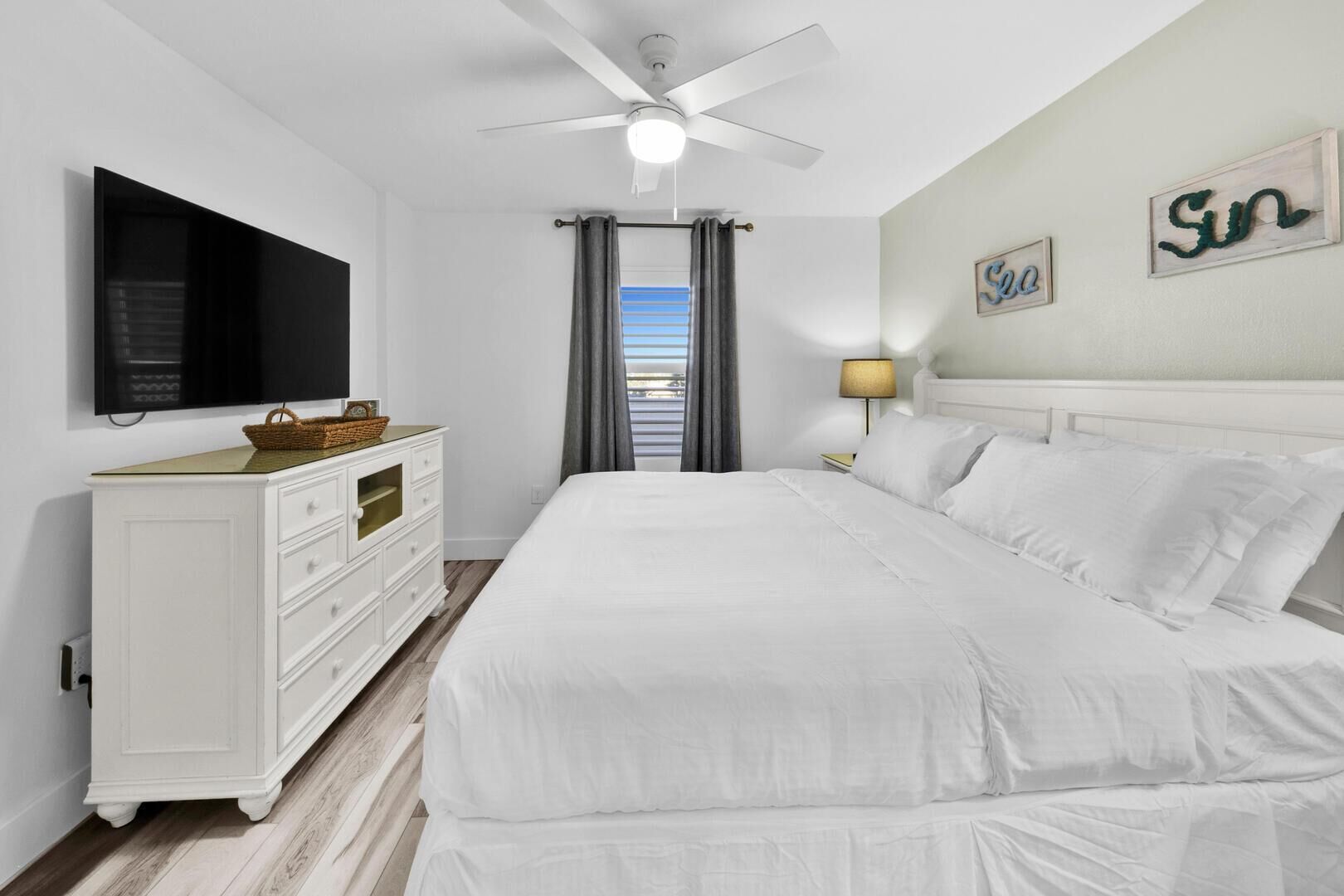 Une chambre d’hôtel avec un grand lit, une commode, un téléviseur et un ventilateur de plafond.