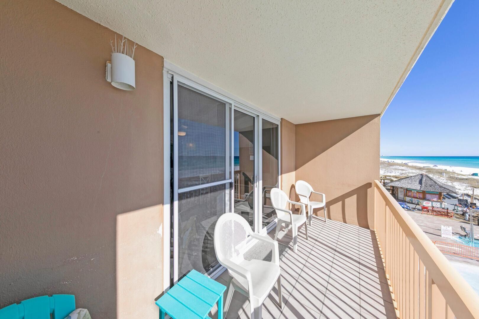 Un balcon avec vue sur la plage, des chaises blanches et une petite table.