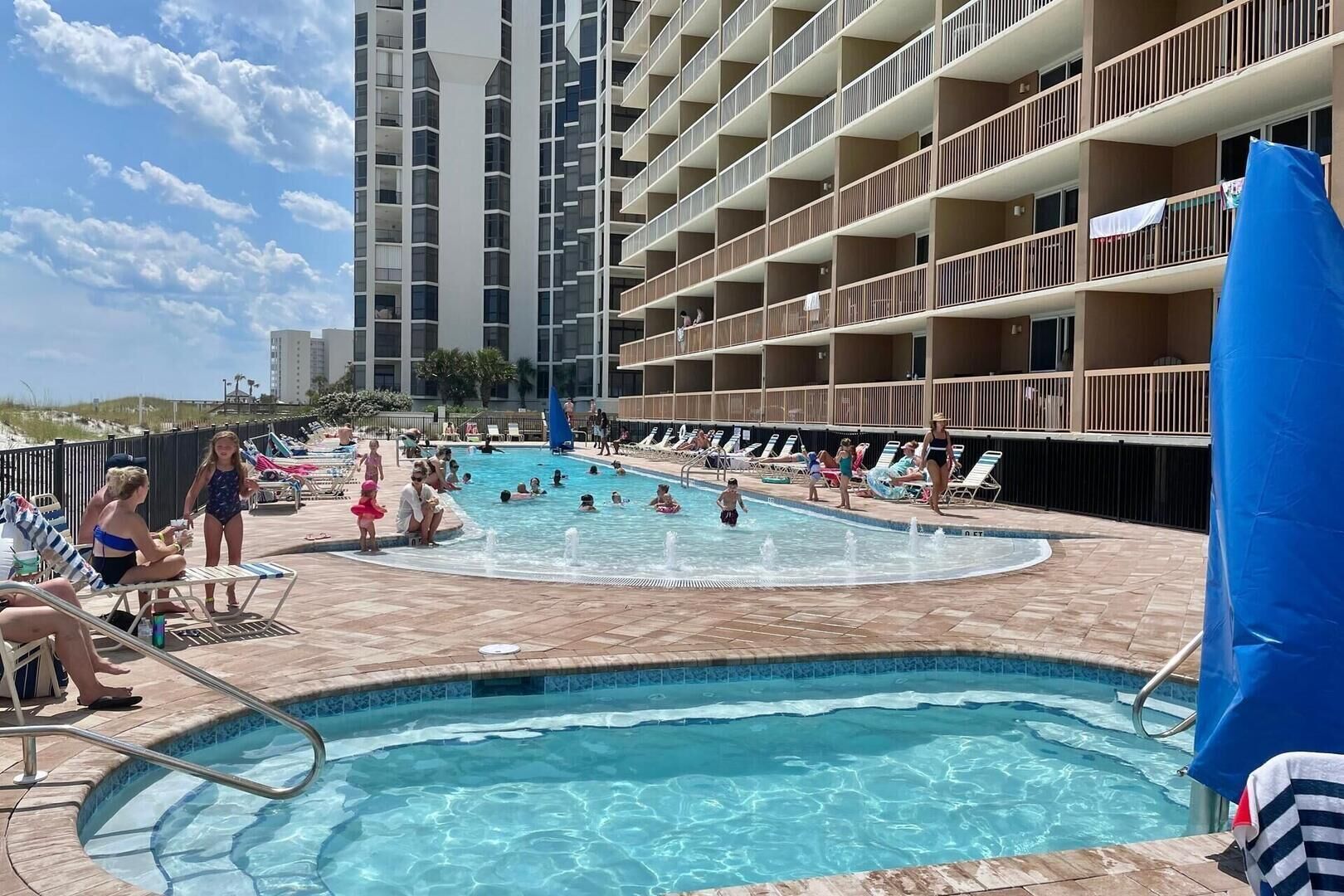A pool area with multiple levels of balconies, a clear sky, and people swimming and relaxing.
