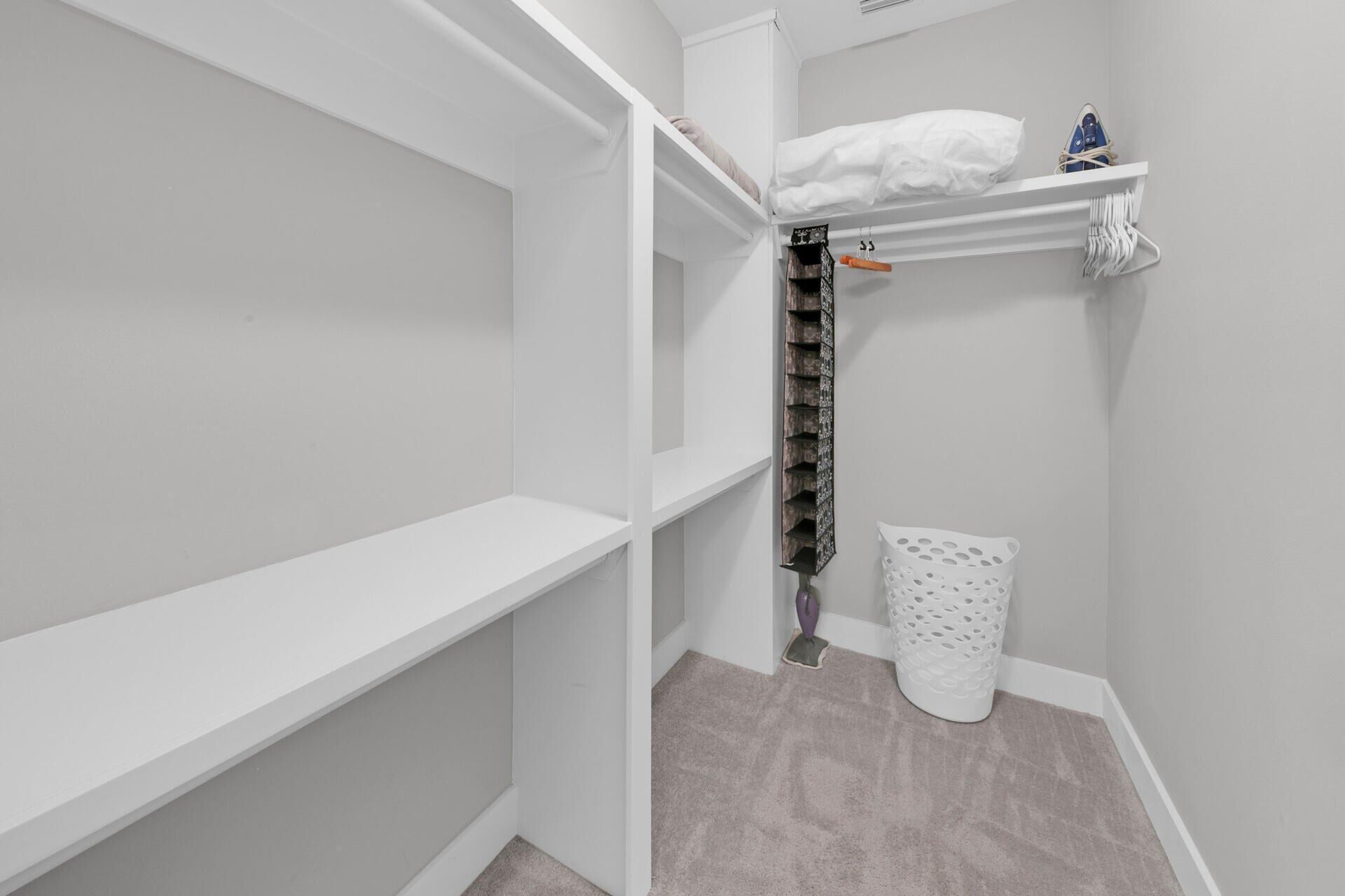 A corner of a room with white walls, a grey carpet, and a white laundry basket.