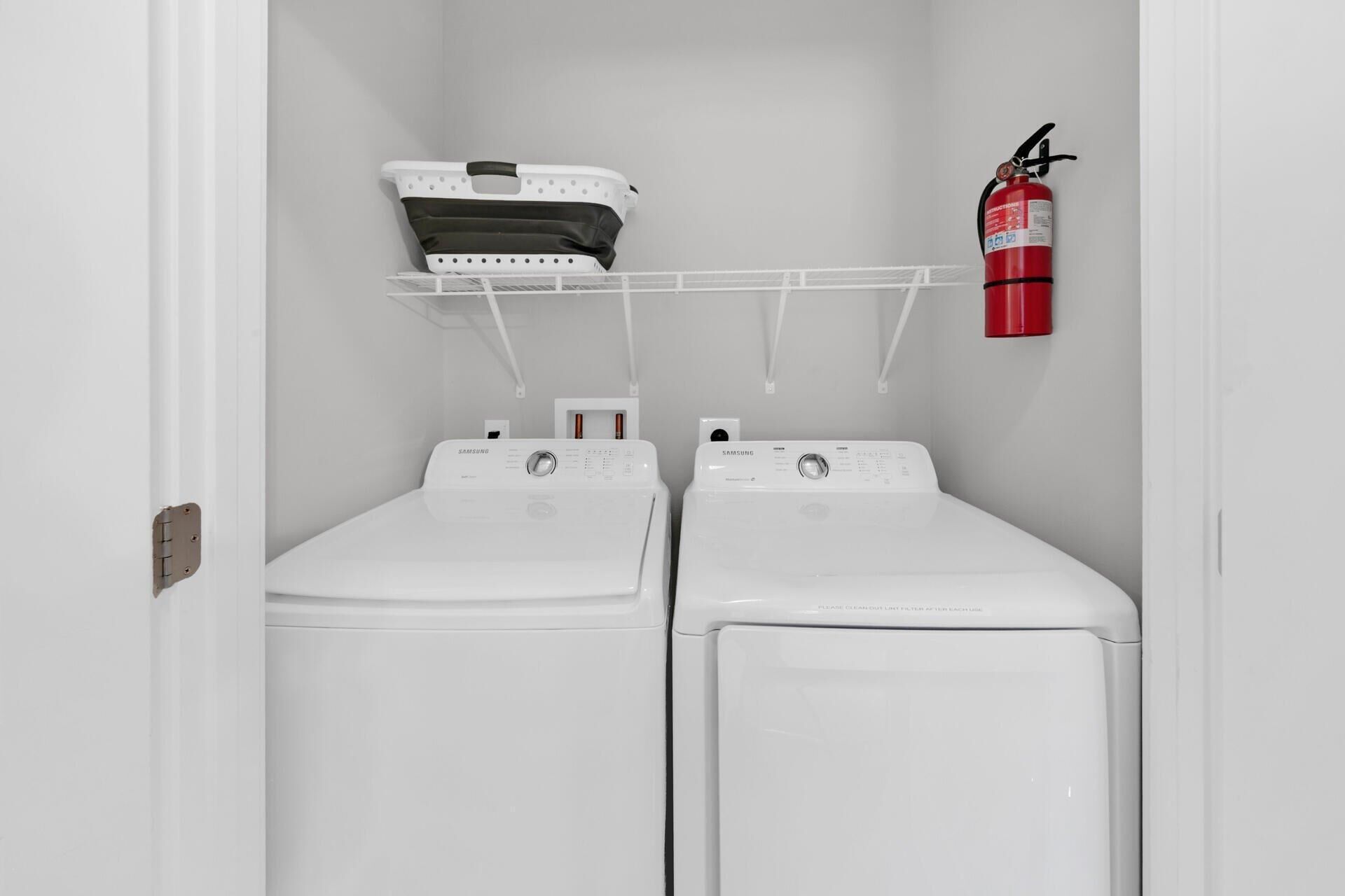 A laundry room with two white front-loading washers and a fire extinguisher mounted on the wall.