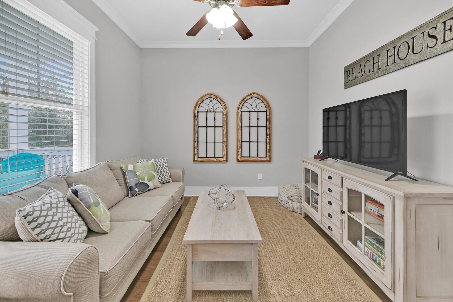 A living room with a sofa, coffee table, TV, and a sign that reads "BEACH HOUSE".
