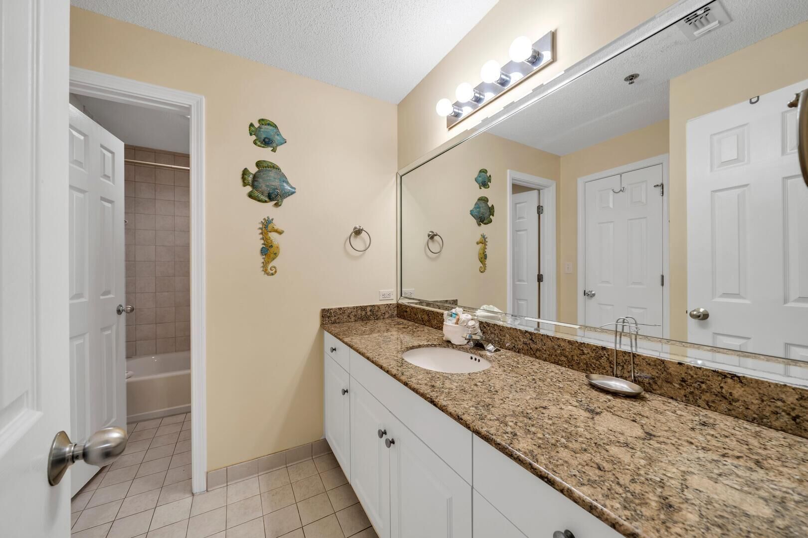 Une salle de bain dotée d’un comptoir en granit, d’un lavabo, d’un miroir avec éclairage intégré et d’une décoration murale représentant des poissons.