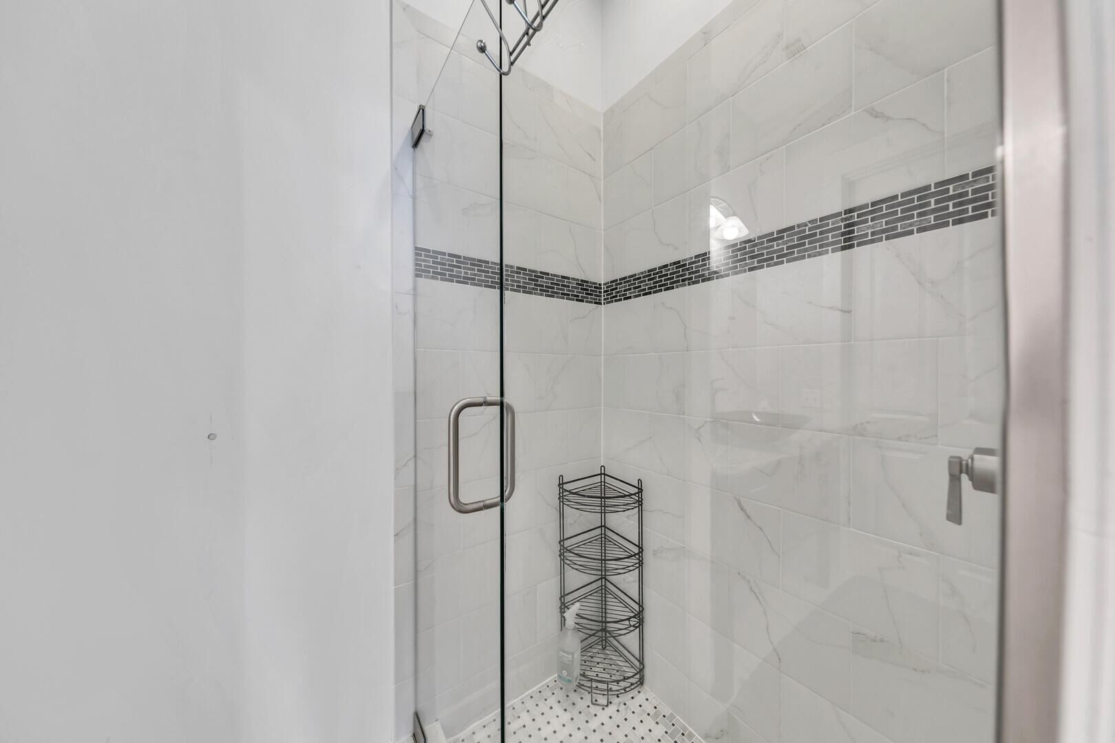 A glass-enclosed shower with white marble tiles and a black-tiled accent wall.