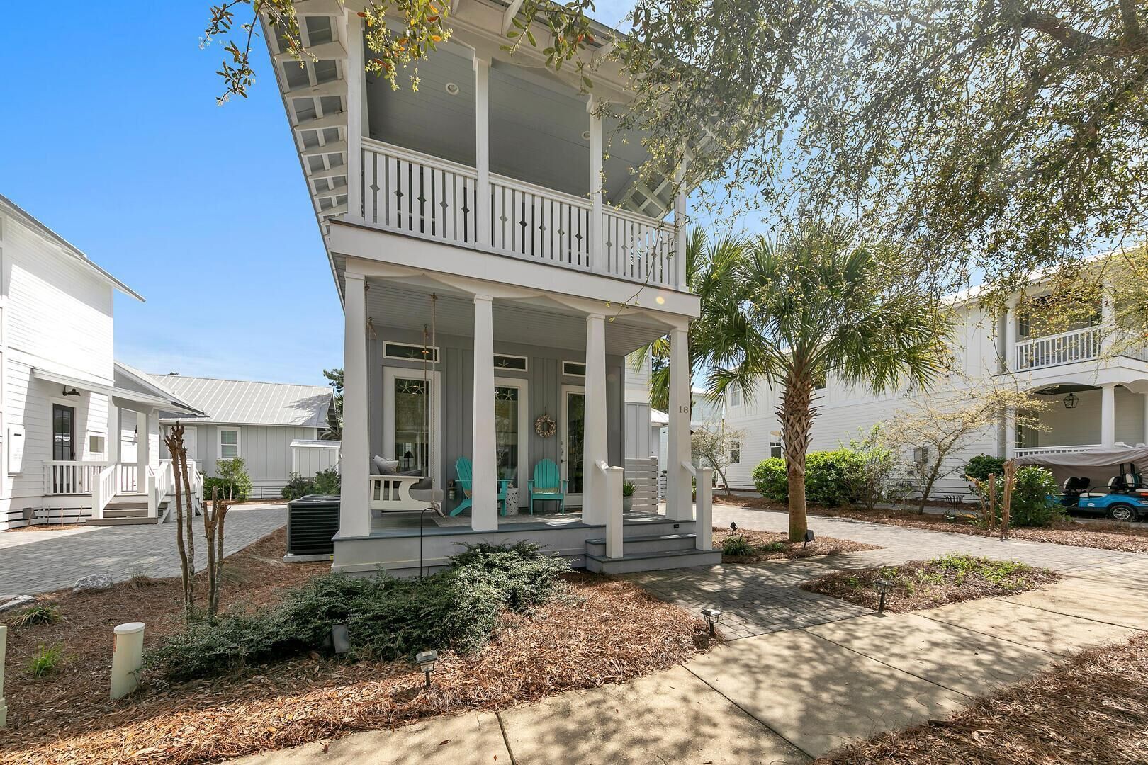 A two-story house with a covered porch, a front door, and a small front yard with a tree and shrubs.