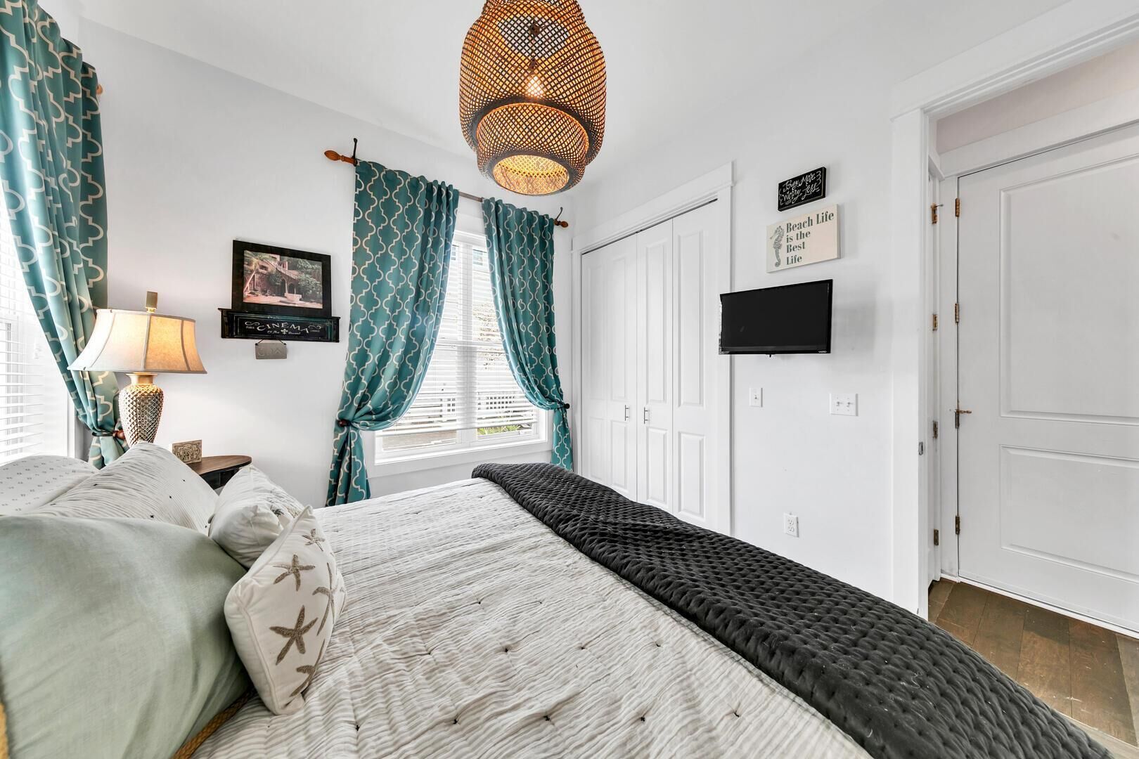 Ein Schlafzimmer mit Bett, Vorhängen, einer Lampe, einem Fernseher und einer Tür.