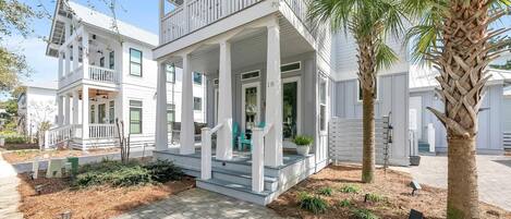 A two-story house with a porch, a balcony, and a palm tree in the yard.