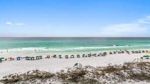 A beach with rows of beach chairs and umbrellas, a sandy shore, and the ocean in the background. - Mainsail 131 (Miramar Beach)