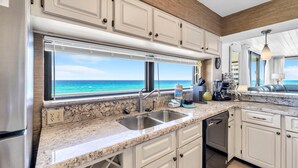 A kitchen with a view of the ocean, a sink, a dishwasher, and white cabinets. - Mainsail 131 (Miramar Beach)