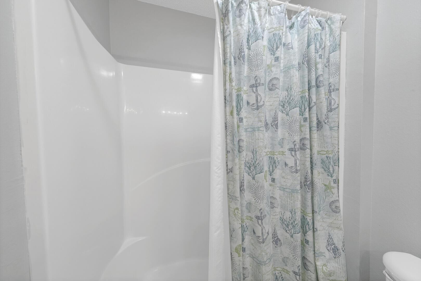 A bathroom with a white shower curtain featuring a nautical pattern, a white toilet, and a white bathtub.