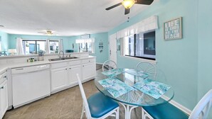 A kitchen with a central island, white cabinetry, a glass dining table with blue chairs, and a ceiling fan. - Crystal Village II, Unit 18A (Miramar Beach)