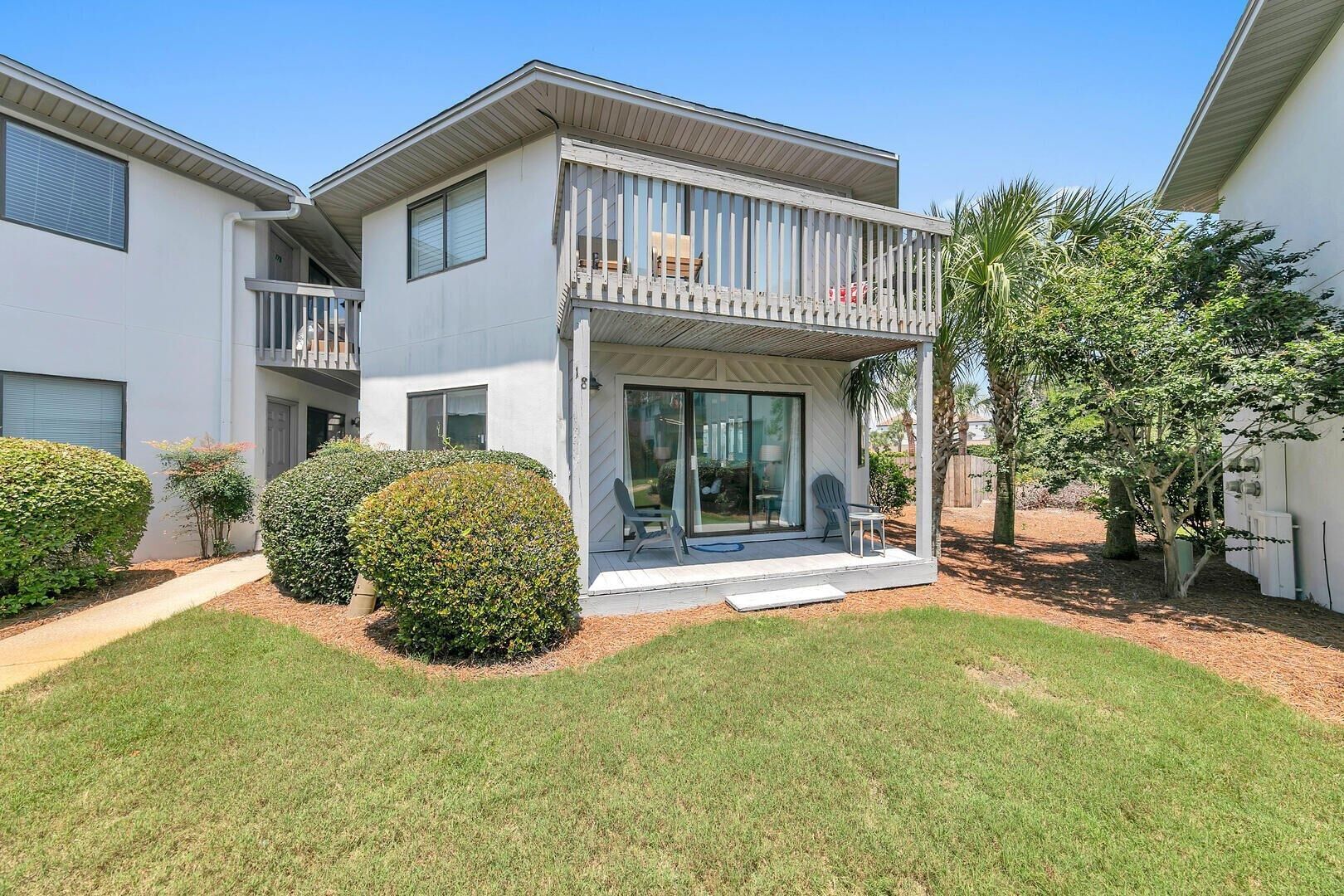 A two-story residential building with a balcony, a covered patio, and a well-maintained lawn.