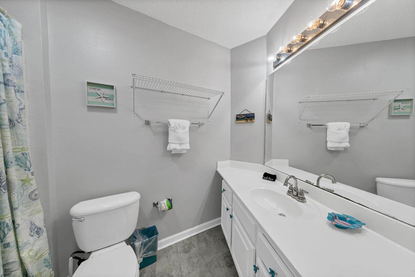A bathroom with a toilet, sink, and mirror. There are towels hanging on hooks and a shower curtain.