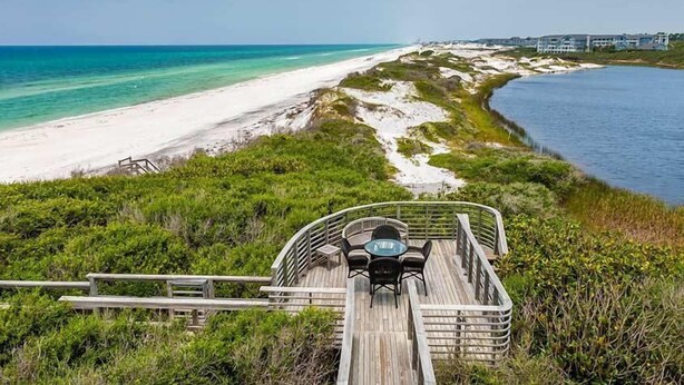 Une terrasse en bois avec une table et des chaises, donnant sur une plage et la mer.