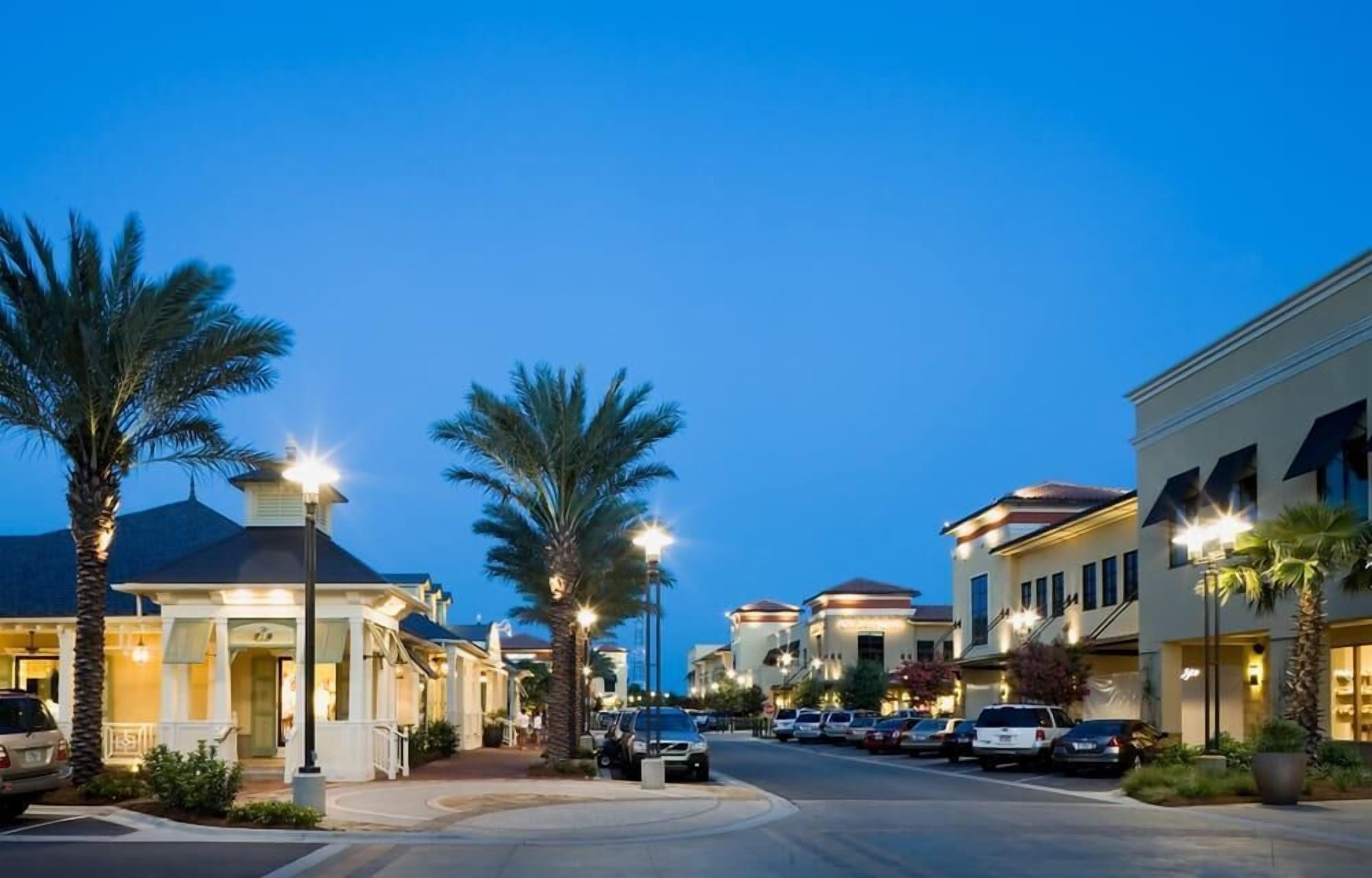 A street lined with palm trees and buildings with warm lighting.