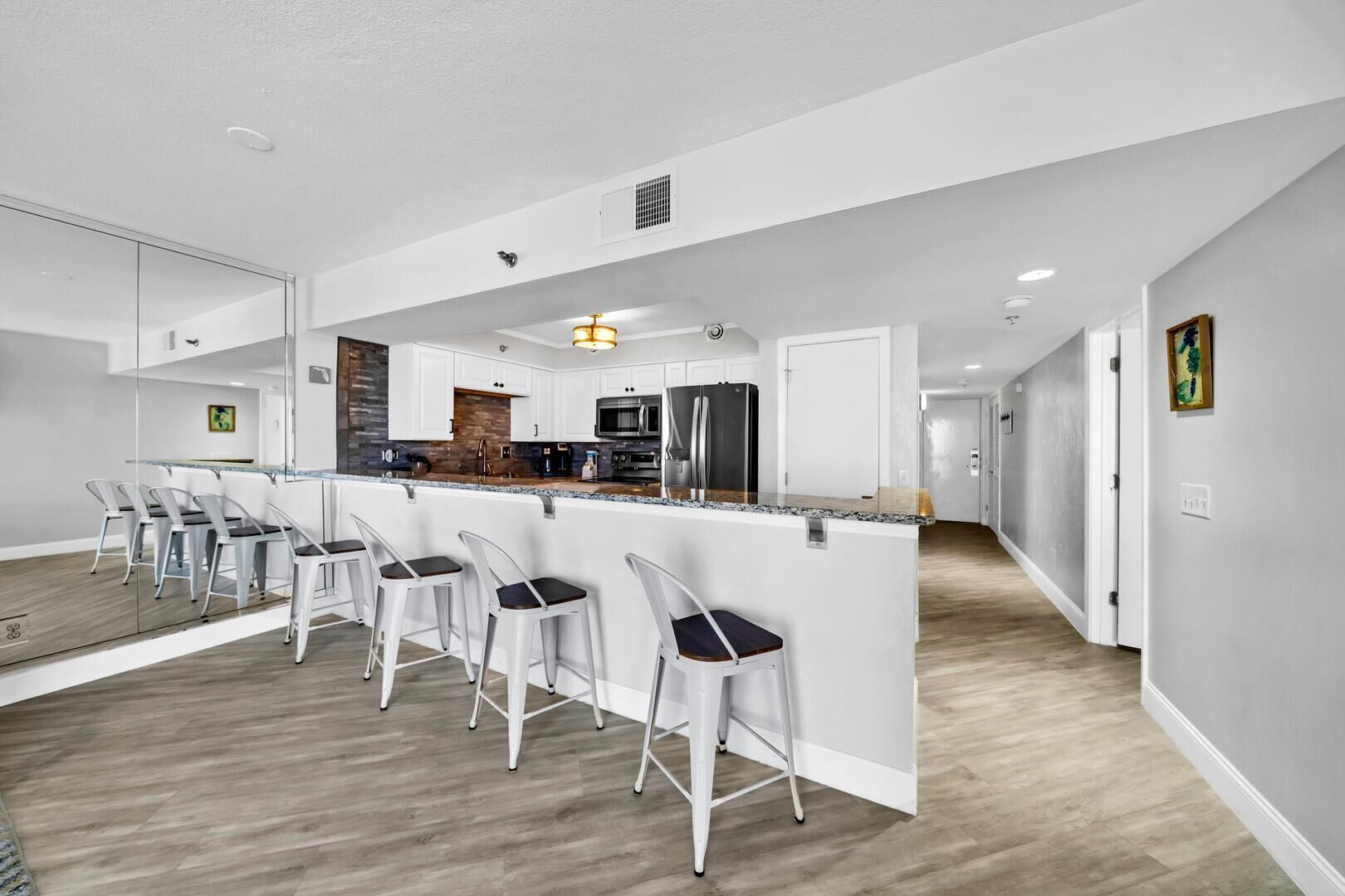 Une cuisine moderne avec des meubles blancs, un îlot central doté de tabourets de bar, des appareils en acier inoxydable et un pare-feu en bois.