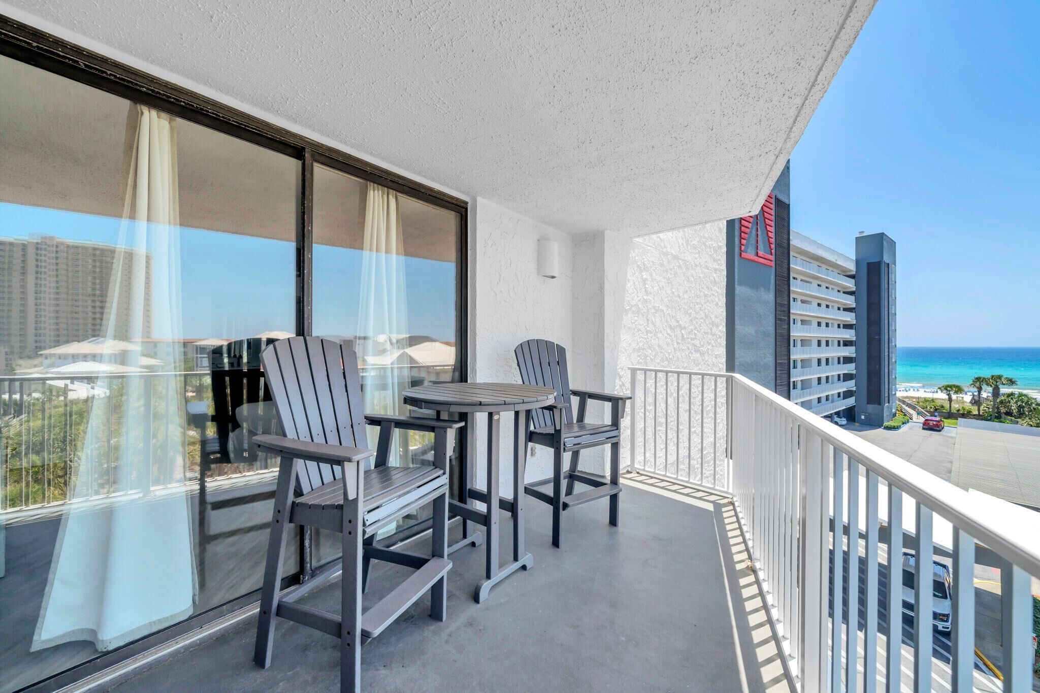 A balcony with a table and chairs, a view of the ocean, and a building with a red and white facade.