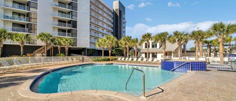 A swimming pool with lounge chairs and palm trees, surrounded by a building with multiple balconies.