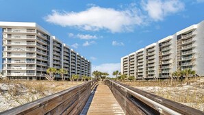 Une promenade en bois mène à un hôtel moderne doté de nombreux balcons, sous un ciel dégagé.
