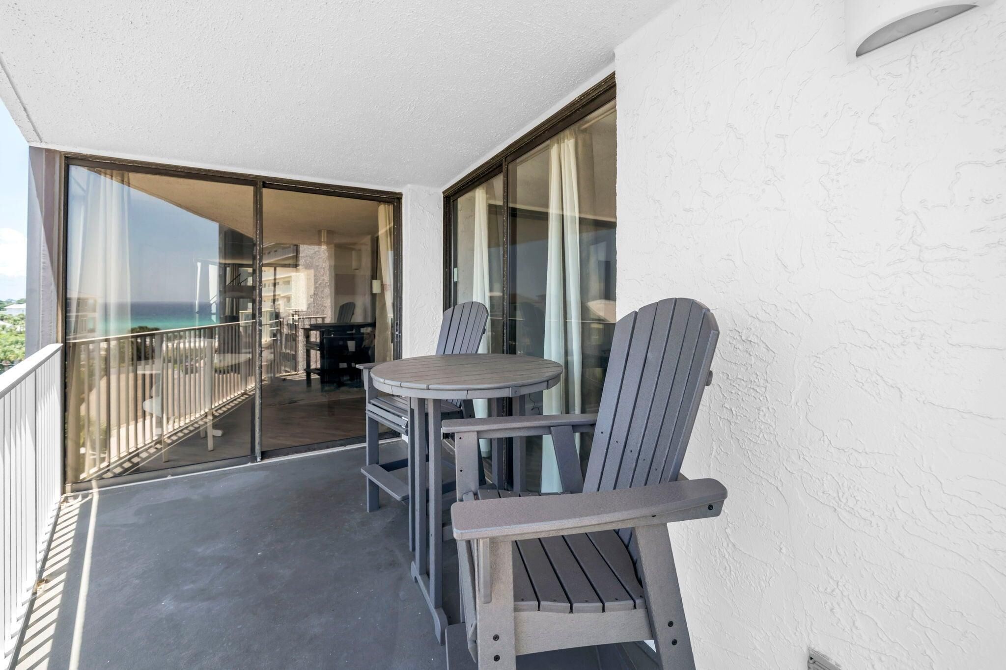 A balcony with a table and chairs, a glass door leading to a room, and a view of the ocean.