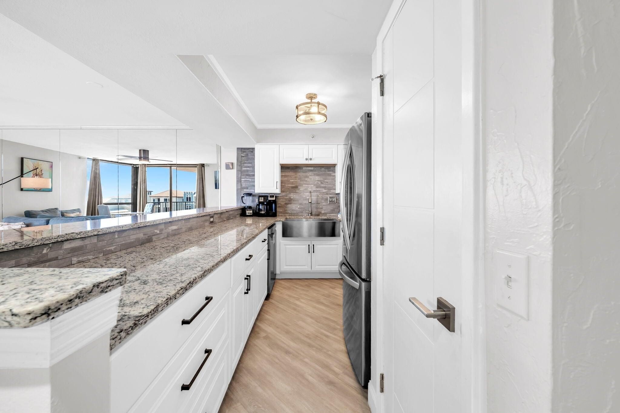 A modern kitchen with white cabinetry, granite countertops, a stainless steel refrigerator, and a coffee maker.