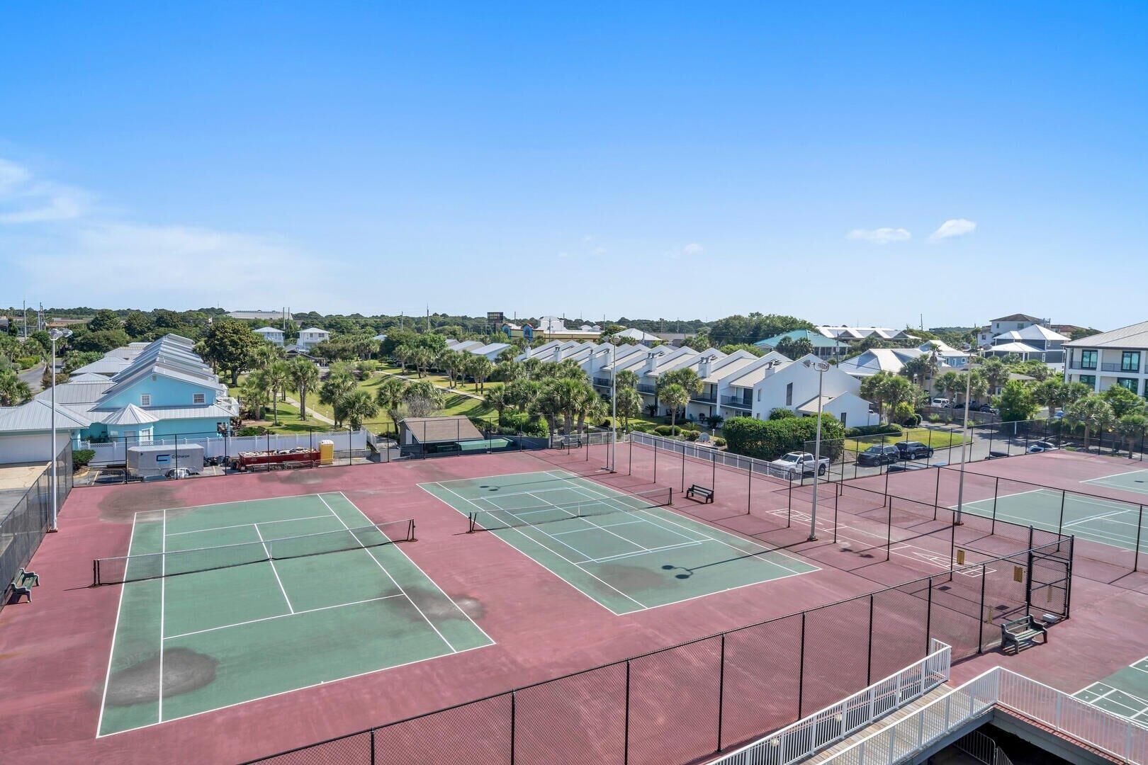 Un complejo de canchas de tenis con varias pistas, rodeado de edificios residenciales y vegetación.