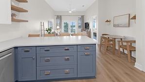 A modern kitchen with a central island, built-in cabinets, and a dining area with wooden chairs and a table. - Emerald by Alma (Santa Rosa Beach)