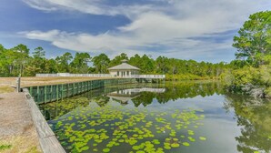 A tranquil lakeside setting with a wooden dock extending into the water, surrounded by lush greenery and a small pavilion. - Emerald by Alma (Santa Rosa Beach)