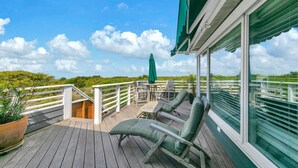 A wooden deck with outdoor furniture, a covered area with a table and chairs, and a view of the landscape. - Henderson Haus (Destin)