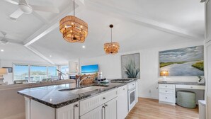 A modern kitchen with a large island, pendant lights, and a painting of a landscape. - Henderson Haus (Destin)