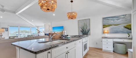A modern kitchen with a large island, pendant lights, and a painting of a landscape.