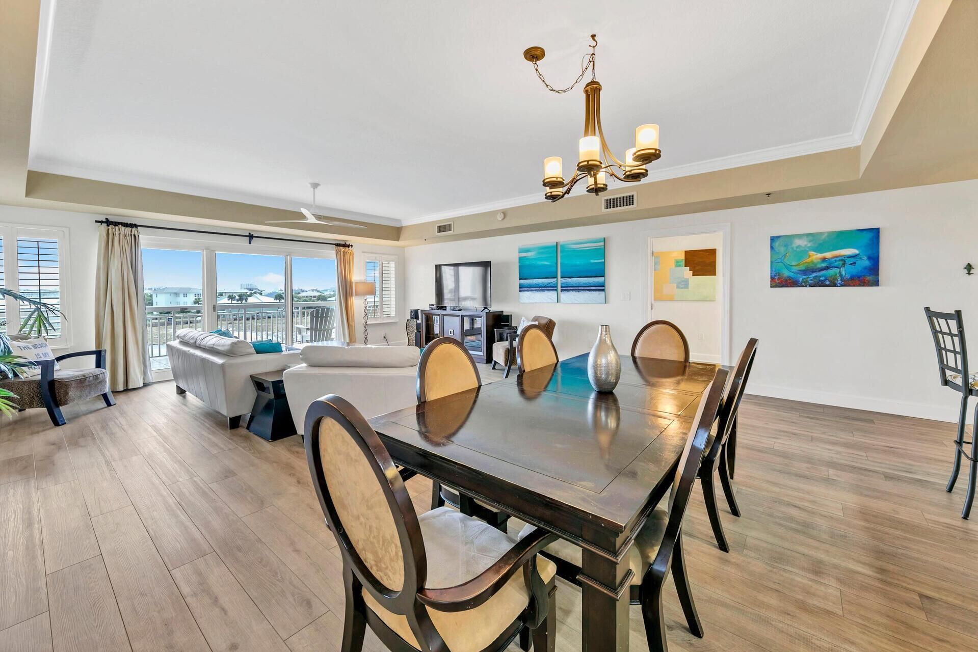 A spacious dining area with a large wooden table and chairs, a chandelier, and artwork on the walls.