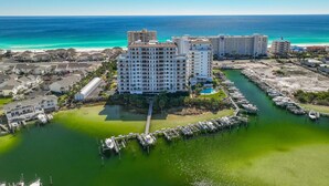 A coastal hotel with multiple buildings, a marina, and a beach in the background. - Harbor Landing 101b (Destin)